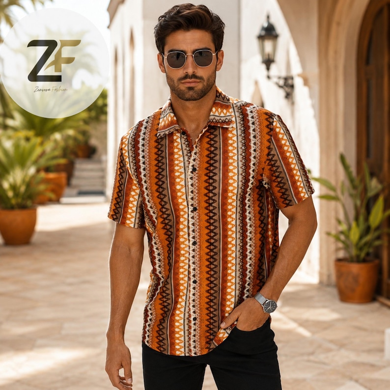 May include: Short-sleeved button-down shirt with a vertical geometric pattern in shades of orange, brown, and white. The shirt is worn with black pants and sunglasses. The logo "ZF Zareena Fashion" is in the upper left corner.