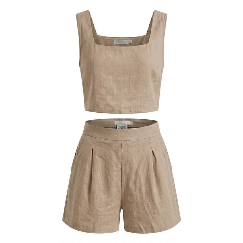 May include: A two-piece beige linen outfit. The set includes a square-neck crop top and high-waisted shorts with pleats. The fabric has a slightly textured appearance.