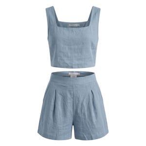 May include: A light blue linen two-piece set. The set includes a square-neck crop top and high-waisted shorts with pleats. The fabric has a slightly textured appearance. The outfit is designed for a casual, warm-weather look.