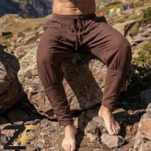 Op de afbeelding: Bruine broek met een elastische tailleband met trekkoord, een relaxte pasvorm bij de bovenbenen en nauwsluitende boorden bij de enkels. De broek is gemaakt van een textuurrijke stof en heeft zichtbare stiksels langs de broekspijpen.