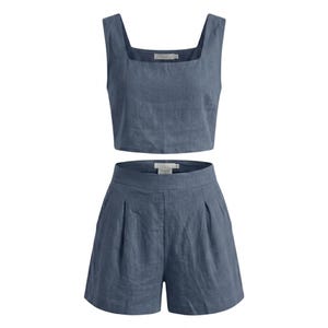 May include: A two-piece set of women's clothing in a dusty blue color. The set includes a crop top with a square neckline and wide straps, and high-waisted shorts with pleats. The fabric appears to be linen or a similar lightweight material.
