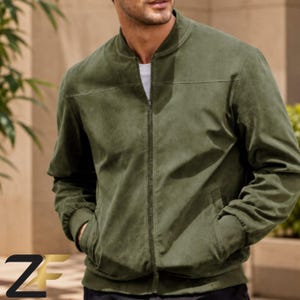 May include: An olive green bomber jacket with a full-length front zipper, a ribbed collar, ribbed cuffs, and two side pockets. The jacket features a horizontal seam across the chest and is worn over a plain white shirt.