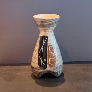 May include: A mid-century ceramic vase with a cream interior and a grey, black, and brown exterior. The vase has a distinctive hourglass shape and abstract black and brown geometric designs.