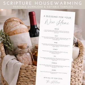 May include: A wicker basket containing a loaf of bread, a bottle of wine, jars of salt and oil, and a printed card with text. The card reads "A Blessing For Your New Home" and includes Bible verses. A sprig of rosemary is in the basket.