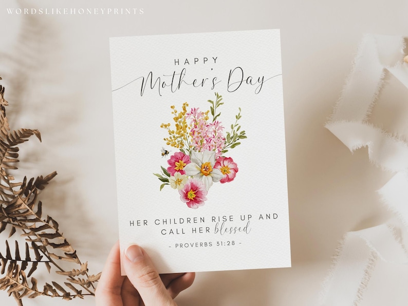 May include: A Mother's Day greeting card with a floral bouquet illustration. The card features the text "Happy Mother's Day" in elegant script, and a quote from Proverbs 31:28. The bouquet includes pink, yellow, and white flowers with green foliage.