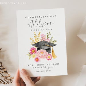Puede incluir: Tarjeta de graduaci&oacute;n con dise&ntilde;o floral y birrete en acuarela. La tarjeta dice "Felicidades Addyson, Clase de 2026" e incluye una cita de Jerem&iacute;as 29:11. Flores rosas y amarillas rodean el birrete.
