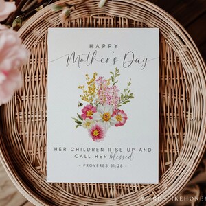 May include: A Mother's Day card with the text "Happy Mother's Day" and a floral bouquet illustration. The card also includes the text "Her children rise up and call her blessed - Proverbs 31:28". The card is on a woven basket.