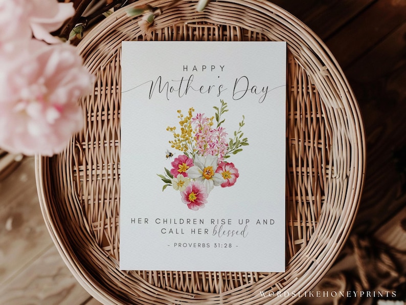 May include: A Mother's Day card with the text "Happy Mother's Day" and a floral bouquet illustration. The card also includes the text "Her children rise up and call her blessed - Proverbs 31:28". The card is on a woven basket.