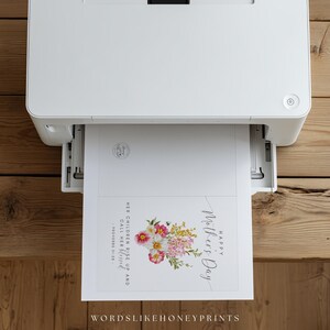 May include: A white printer printing a Mother's Day card. The card features a floral arrangement with pink, yellow, and white flowers, along with the text "Happy Mother's Day". The card also includes the text "Her children rise up and call her blessed".