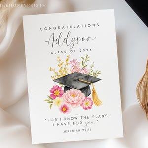Puede incluir: Tarjeta de graduaci&oacute;n con el nombre "Addyson" y "Clase de 2026" en escritura elegante. La tarjeta presenta una ilustraci&oacute;n de acuarela de un birrete, flores y una borla. Tambi&eacute;n se incluye la cita "Porque yo s&eacute; los planes que tengo para vosotros".