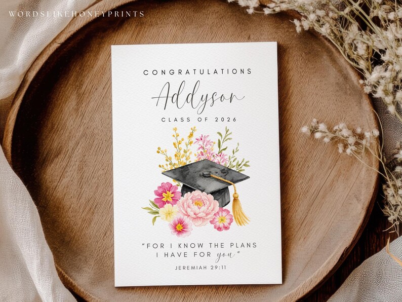 Puede incluir: Tarjeta de graduaci&oacute;n con el nombre "Addyson" y el a&ntilde;o "2026". La tarjeta presenta una ilustraci&oacute;n en acuarela de un birrete, flores y la cita "Porque yo s&eacute; los planes que tengo para vosotros" de Jerem&iacute;as 29:11.