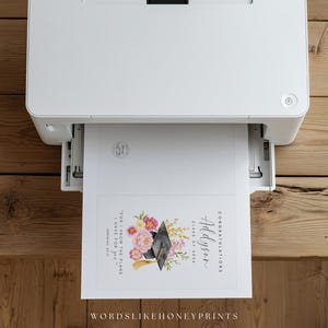 Puede incluir: Una impresora blanca imprimiendo un anuncio de graduaci&oacute;n. El anuncio presenta un dise&ntilde;o floral con flores rosas y amarillas, un birrete negro y el nombre "Addyson". Tambi&eacute;n se ve el texto "Felicitaciones" y "Clase de 2024".