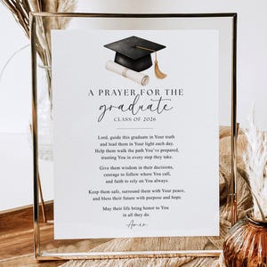 May include: A framed graduation prayer card. The card features a watercolor illustration of a graduation cap and diploma. Text includes "A Prayer for the Graduate, Class of 2026" and a prayer.