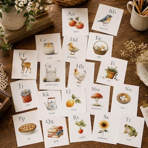 Könnte beinhalten: Ein Set aus zwanzig pädagogischen Alphabetkarten mit Aquarellillustrationen und dem entsprechenden Text für jeden Buchstaben von A bis T, darunter Bilder von Apfel, Blauvogel, Kerze, Entenküken, Eiern, Rehkitz, Gartentor, Henne, Efeu, Marmelade, Wasserkocher, Zitrone, Pilz, Nest, Kuchen, Steppdecke, Radieschen, Sonnenblume und Kröte.