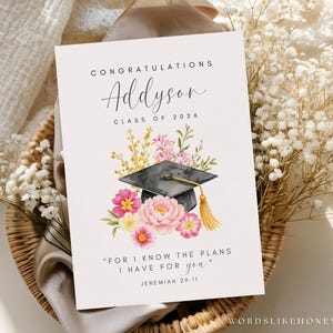 Puede incluir: Tarjeta de graduaci&oacute;n con el nombre "Addyson" y "Clase de 2026" en escritura elegante. La tarjeta presenta una ilustraci&oacute;n de acuarela de un birrete, flores y la cita "Porque yo s&eacute; los planes que tengo para vosotros" de Jerem&iacute;as 29:11.