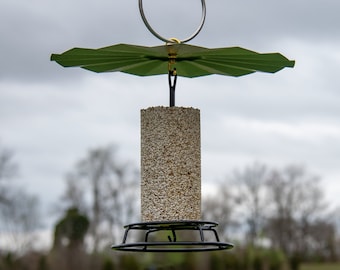 May include: A hanging bird feeder with a green, scalloped roof and a cylindrical seed container. The feeder has a black wire base and a metal hook for hanging. The seed container is filled with birdseed.
