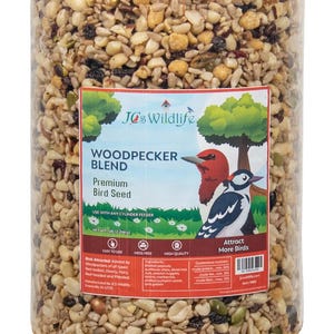 Könnte beinhalten: Ein transparenter Plastikzylinder gefüllt mit einer Mischung aus Vogelsamen für Spechte. Das Etikett lautet "JCs Wildlife Woodpecker Blend Premium Bird Seed" und zeigt eine Illustration eines Rotkopfspechts. Das Etikett enthält auch die Hinweise "Verwenden Sie jeden Zylinder-Futterspender" und "Nettogewicht 5 lb (2,26 kg)".