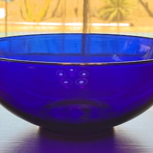 Puede incluir: Un cuenco circular grande y profundo hecho de vidrio azul cobalto translúcido. El cuenco presenta una superficie lisa y pulida con una parte superior ancha y abierta y una base redondeada, reflejando la luz en su color azul vibrante.
