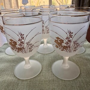 Op de afbeelding: Een set frosted glazen kelken met een bruin bloemmotief en een gouden rand. De kelken hebben een brede, ovale voet en een slanke steel. Het ontwerp herhaalt zich op elk glas.