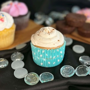 May include: A close-up of several cupcakes with white frosting and colorful sprinkles. One cupcake has a light blue and white polka dot liner. Other cupcakes and brownies are in the background.