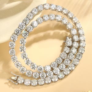 May include: A dazzling, silver-toned tennis necklace featuring numerous round, clear gemstones. The necklace is arranged in a curved pattern, showcasing the sparkling stones and the clasp.