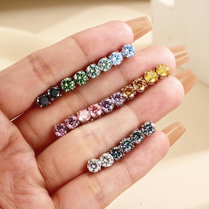 May include: Three linear rows of round-cut gemstones set in metal. The top row features black, green, and blue stones. The middle row displays pink, purple, and yellow stones. The bottom row contains clear and dark gray stones.