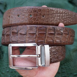 Peut inclure: Une ceinture en cuir marron avec un motif de crocodile textur&eacute;. La ceinture a une boucle argent&eacute;e. La ceinture est enroul&eacute;e, montrant la texture et la couleur du cuir. Accessoire de mode.