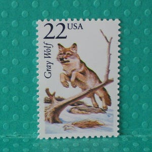 May include: A 22-cent USA postage stamp featuring a gray wolf leaping over a fallen tree. The stamp has a white background with the text "Gray Wolf" and "USA". The wolf is depicted in shades of brown and gray.