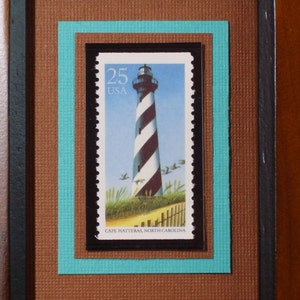 Könnte beinhalten: Eine alte 25-Cent-Briefmarke der USA mit einem schwarz-weiß gestreiften Leuchtturm mit dem Text "Cape Hatteras, North Carolina".