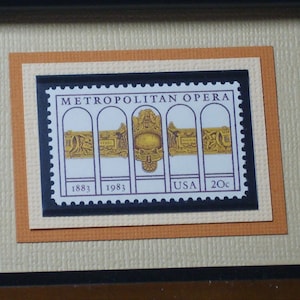 Peut inclure: Un timbre-poste américain de 20 cents encadré commémorant le 100e anniversaire du Metropolitan Opera en 1983. Le timbre présente un motif doré avec le texte "Metropolitan Opera" et les années "1883" et "1983".