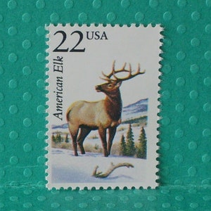 May include: A 22 cent USA postage stamp featuring a brown and tan American Elk with large antlers standing in a snowy forest setting.