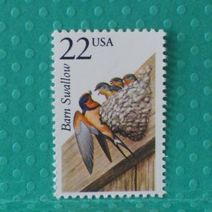 May include: A 22 cent USA postage stamp featuring a barn swallow perched on a wooden surface with a nest of baby swallows. The stamp is a light blue color with white text.