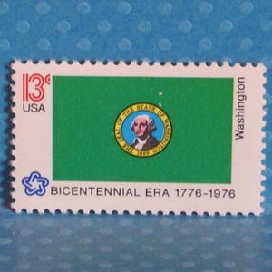 Op de afbeelding: Een rechthoekige postzegel met het ontwerp van de vlag van de staat Washington. De postzegel heeft een groene achtergrond met een cirkelvormig embleem van George Washington. De tekst "13¢ USA" en "Washington" zijn zichtbaar. De postzegel herdenkt de Bicentennial Era 1776-1976.