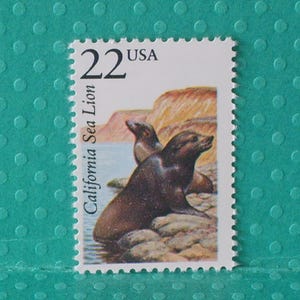 May include: A vintage postage stamp featuring two California sea lions on a rocky shore. The stamp has a 22-cent value and the text "USA" at the top. The words "California Sea Lion" are printed vertically on the left side.