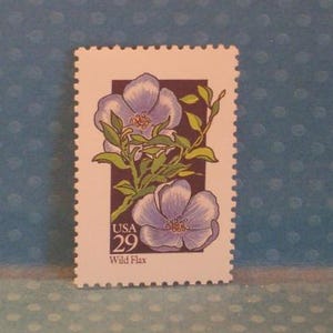 Puede incluir: Un sello postal de EE. UU. con dos flores de lino silvestre de color púrpura claro con hojas y tallos verdes. El sello tiene un borde blanco con un borde perforado y el número 29 en la esquina inferior izquierda.