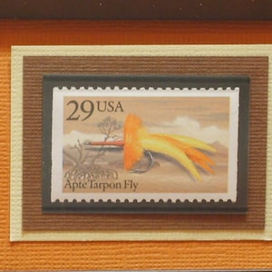 Può includere: Un francobollo americano vintage con un valore di 29 centesimi e una rappresentazione colorata di una mosca Apte Tarpon Fly. Il francobollo è incorniciato in un passepartout marrone e crema.