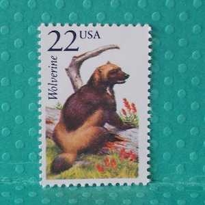 May include: A vintage 22-cent USA postage stamp featuring a wolverine. The stamp depicts a brown and tan wolverine sitting on a log with red flowers and a tree branch in the background. The word "Wolverine" is printed vertically.
