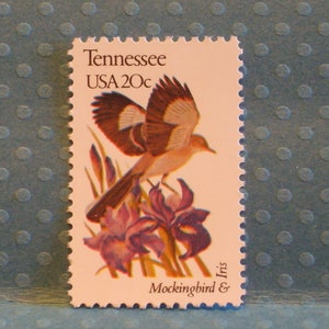 May include: A vintage United States postage stamp featuring a brown and white mockingbird perched on a purple iris flower. The stamp is labeled "Tennessee USA 20c Mockingbird & Iris".