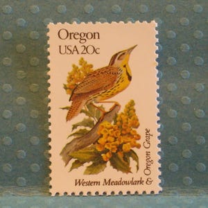 May include: A vintage postage stamp from Oregon, USA, featuring a Western Meadowlark perched on a branch with yellow flowers. The stamp is white with a serrated edge and the text "Oregon USA 20c".