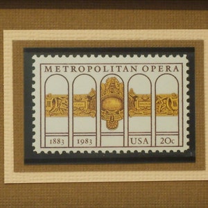 Peut inclure: Un timbre-poste américain vintage de 20 cents représentant le Metropolitan Opera House de New York. Le timbre est en noir et blanc avec un motif doré et le texte "Metropolitan Opera" et "USA 20c".