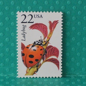 May include: A US postage stamp featuring a ladybug on a plant with the text "22 USA Ladybug" printed on the stamp.