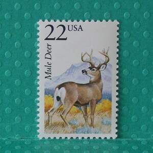 May include: A 22 cent USA postage stamp featuring a brown and white mule deer with large antlers standing in a grassy field with a mountain in the background.