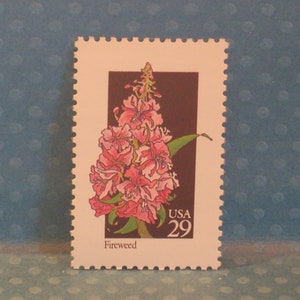 Puede incluir: Un sello postal estadounidense vintage con una flor rosa de Fireweed con hojas verdes sobre un fondo marrón. El sello está etiquetado como "USA 29" y "Fireweed".