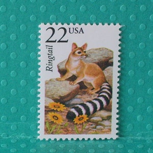 May include: A postage stamp featuring a Ringtail animal. The stamp has a value of 22 cents and the text "USA". The Ringtail is depicted on rocks with a black and white striped tail and yellow flowers.