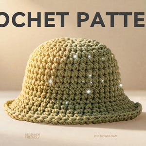 Peut inclure: Un chapeau seau crocheté vert olive clair. Le chapeau présente un motif de point visible et un bord légèrement évasé. Le texte "CROCHET PATTERN" est visible. Le patron est adapté aux débutants.