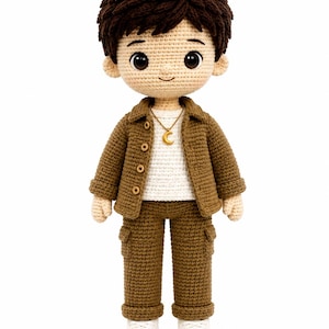 May include: A handmade crochet doll with dark brown hair, wearing a brown button-up jacket over a white shirt, brown trousers, and white sneakers. The doll features a gold-colored crescent moon pendant necklace and has large, dark, round eyes.