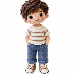Puede incluir: Una muñeca de ganchillo hecha a mano con pelo de hilo marrón, que viste una camiseta de manga corta color crema con rayas horizontales marrones, pantalones azules con dobladillo y zapatillas beige con cordones blancos, en punto texturizado.