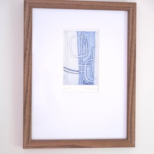 Op de afbeelding: Ingelijste abstracte kunstprint met een blauw en wit geometrisch ontwerp. Het kunstwerk is rechthoekig, geplaatst in een witte passe-partout en een bruine houten lijst. De print heeft een moderne uitstraling.