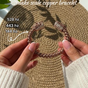 May include: Copper bracelet with a snake scale design. The bracelet is a twisted rope style with a copper finish and silver-colored accents. The text "Snake scale copper bracelet" is visible in the image.