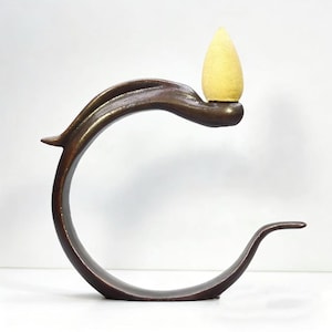 May include: A bronze incense holder with a curved, leaf-like design. It holds a yellow incense cone. The holder's organic shape is suitable for home decor and aromatherapy, adding a touch of nature.